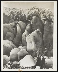 Famous New Zealand Glacier. Tourists photographed as they stood beside the great blocks of ice on Fox Glacier, South Westland, in New Zealand. The glacier attracts visitors from all parts of the world and is distinguished by the peculiar formations it assumes, altogether unusual from the usual formations of glacial ice. Note the great height of these blocks in comparison to the tourists.