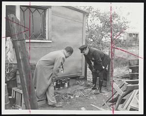 Lethal Stuff- Special Officer Ralph Mele and Revere Officer Vincent O'Hara inspect hideout under shack behind 183 Malden street, Revere, where jugs of liquor were found which may be linked to alcohol poison deaths.