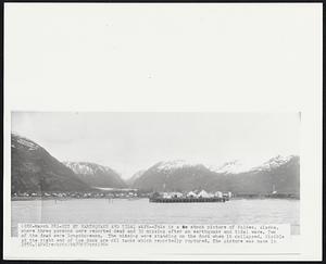 Hit by Earthquake and Tidal Wave--This is a stock picture of Valdez, Alaska, where three persons were reported dead and 30 missing after an earthquake and tidal wave. Two of the dead were longshoremen. The missing were standing on the dock when it collapsed. Visible at the right end of the dock are oil tanks which reportedly ruptured. The picture was made in 1950.
