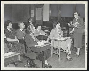 How To Pronounce is taught by example as Mrs. George Mann, teacher at the School of Newcomers, conductor by the Boston Section, National Council of Jewish Women, holds a class of DP’s. At left in rear are Mr. and Mrs. Arthur Plaut, who met as students at the school in Brookline and were married in July. Others: Mrs. Ellen Hollander, Mrs. Max Alexander and Mrs. Fred Godel, all students.
