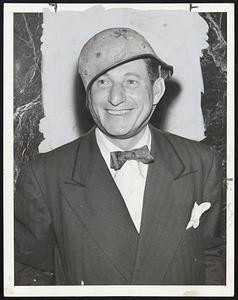 Clown in a Coal-Scuttle-Al Schacht famous baseball comedian recently returned from an entertainment tour of North Africa, beams from beneath a captured German "coal-scuttle" helmet presented him by a tanks corp colonel. Schacht, who entertained 450,000 soldiers, says he was bombed four nights in a row.
