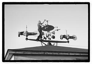 A man adjusting an elaborate device on roof, possibly a weather vane