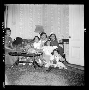 A woman is seated on couch with four girls, another woman seated farther to the left