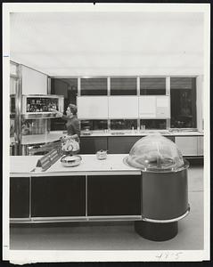 Cooking, food preparation, cleaning and planning centers of the all-new Frigidaire Kitchen of Tomorrow are shown here. Attractive young homemaker demonstrates unusual refrigerator in left background.