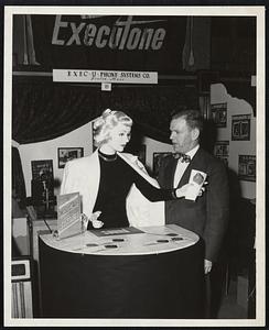 Jim McTaggert, Chairman of the Business Show of the Boston Chapter of the National Association of cost accountants at  the Horticultural Hall now, is shown interviewing "Miss Tone", talking mannequin who is made of plaster and is wired for sound. No dummy this dummy? Her eyes and lips move as she carries on a livery patter about the Executone inter-office communication system being exhibited there.
