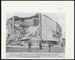 Troops Patrol Stricken Alaskan City -- With the city under martial law, soldiers patrol a downtown street in Anchorage, Alaska today. In background is the wreckage of the five-story Penney store at Fifth Avenue and D street.