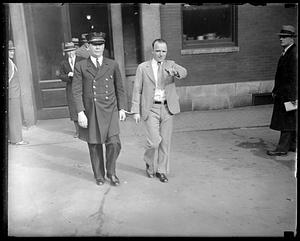 A man handcuffed to a police officer points