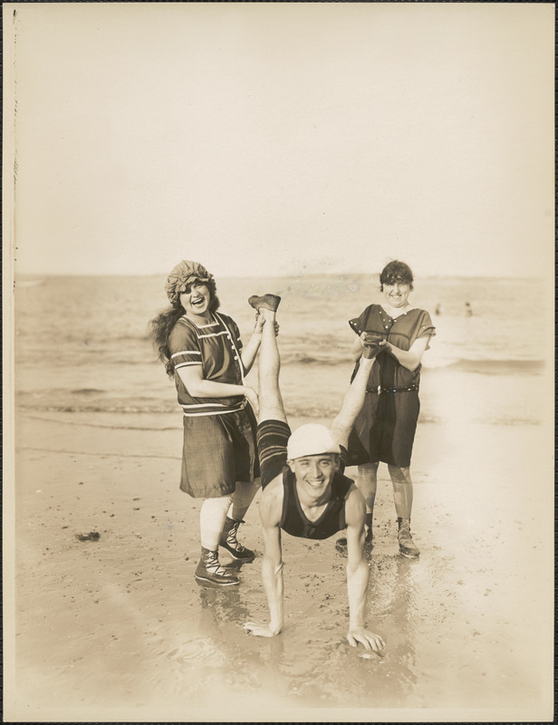 Two women holding up legs of man on beach
