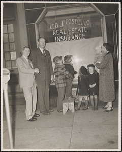 Leo J. Costello shaking the hand of Thomas F. Hughes, the Costello family standing to their right