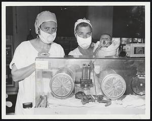 Fight for Life--Weighing only one pound, eight ounces, a baby known as "Phillip" remains under constant care in Isolette at New England Hospital in Roxbury. He is five days old today. Mrs. Hazel Sword caresses Phillip's head while Miss Dorothy Denehy holds up nine-pound, four ounce Susan Goss. Phillip weighed one pound, 12 ounces at birth, is fed by a stomach tube.
