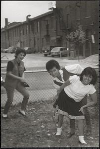 Three women, one a teenager, laughing and posing in front of a fence