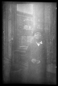 A boy wearing a hat stands in front of a storefront