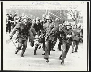 Riot garbed State Police carry a rock throwing demonstrator to waiting bus after catching him near center campus of Penn State University.