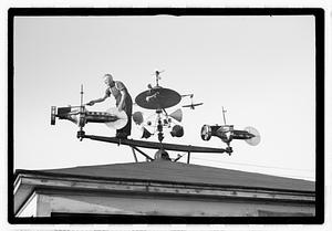 A man adjusting an elaborate device on roof, possibly a weather vane