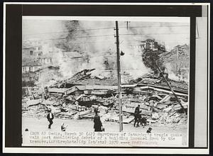 Survivors of Saturday's tragic quake walk past smouldering debris of a building knocked down by the tremors.