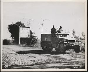 An armored reconnaissance car speeds past a [Japanese] road sign along the main highway to San Miguel, Luzon Island