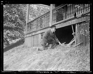 Police officer kneels by a hole made underneath a porch of a building