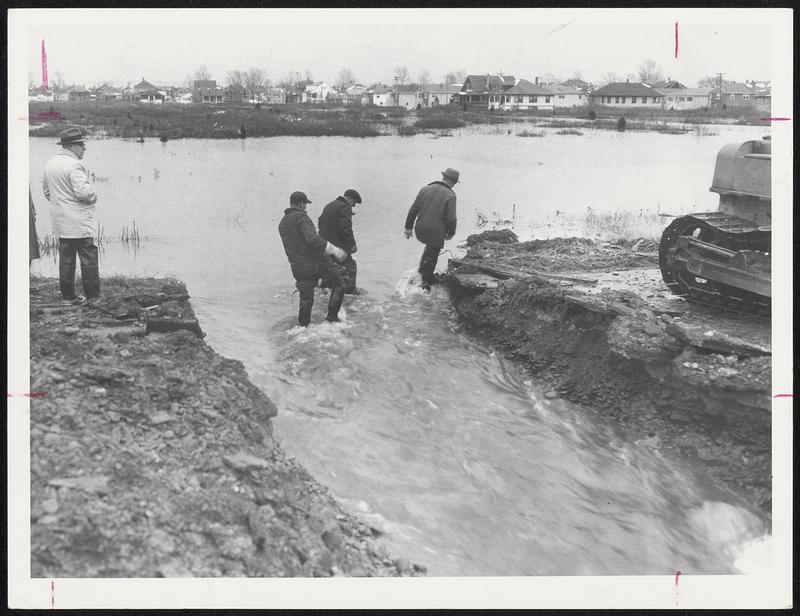 Breaking the Dike-Hull Highway Dept. employees wade through the sluiceway created when they used a bulldozer to open the sea wall which was keeping sea water in the flooded Kenberma sction. Selectman Hugh Ross is at left.