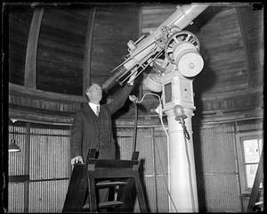 A man gesturing to a large telescope