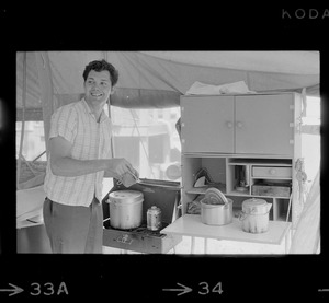 Tom Hinds in a tent in front of cook stove