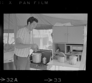 Tom Hinds in a tent in front of cook stove
