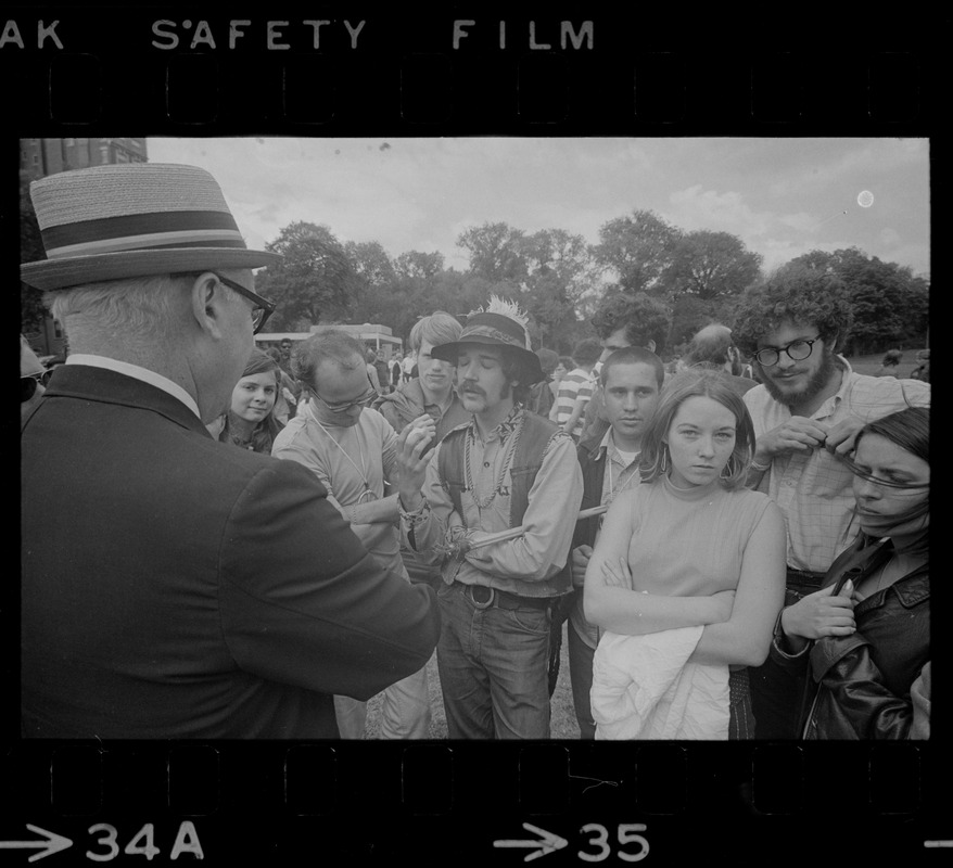 Man with a hat speaking to a group of hippies on the Boston Common