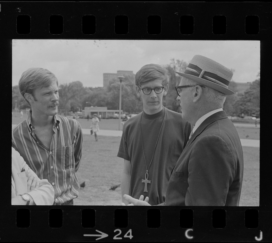 Man with a hat speaking to a group of hippies on the Boston Common