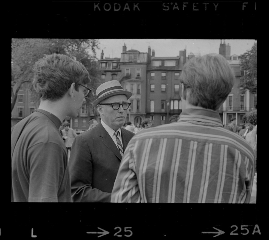 Man with a hat speaking to a group of hippies on the Boston Common