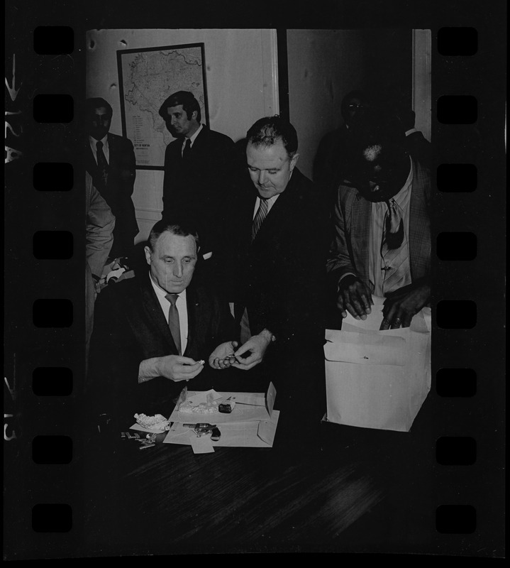 Lt. William J. Gross of State Police Narcotics Unit, seated, and Newton police chief William Quinn, standing center, inspecting items with others