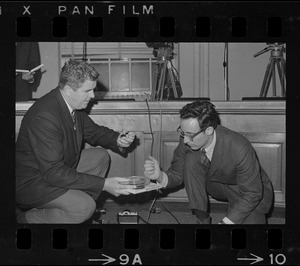 Titicut Follies' hearing taped - Timothy Asch, (right), Cambridge, turns over rolls of film and tape recording to Sgt.-at-Arms John J. Cavanaugh, after it was discovered the "Titicut Follies" hearing at the State House was being recorded