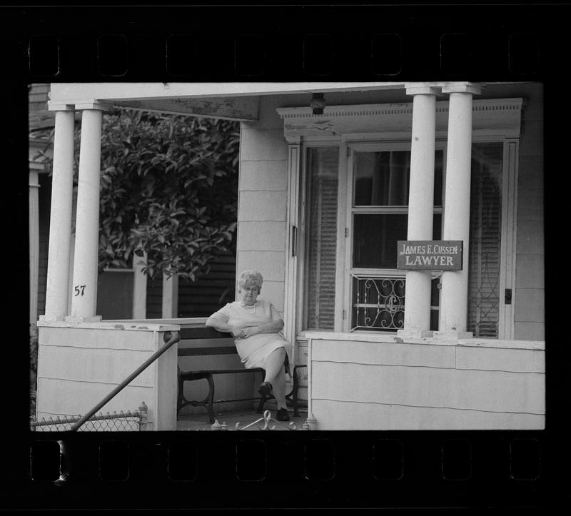 Woman on bench next to a sign for James E. Cussen, lawyer, Dorchester