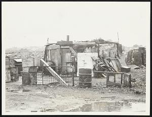 A de luxe squatters' shack in the more exclusive part of Dorchester's shantytown. In the right rear is one of the lower class dwellings, made of old standing against each other.