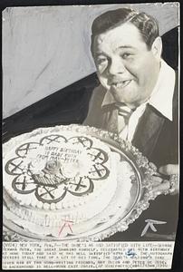 The Babe's 46 And Satisfied With Life -- George Herman Ruth, the great Bambino himself, celebrated his 46th birthday at home today and said he was well satisfied with life. The autograph seekers still take up a lot of his time. The Babe's holding a cake given him by two song-writing friends, May Breen and Peter De Rose. In background is well-worn easy chair.