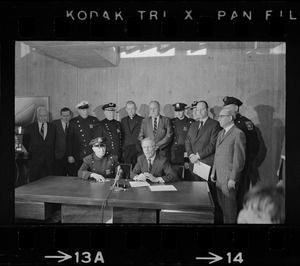 Police Patrolmen's Association President Daniel Sweeney and Mayor Kevin White signing new wage package for Boston Police. In background left to right, two unidentified men, Officer Ray Winston, Deputy Supt. William Bradley, Rev. James Lane, Com. Edmund McNamara, Patrolman Paul Whelan, Superintendent-in-Chief William Taylor, Attorney Robert Wise, and two unidentified men