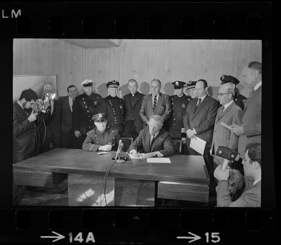 Police Patrolmen's Association President Daniel Sweeney and Mayor Kevin White signing new wage package for Boston Police. In background left to right, two unidentified men, Officer Ray Winston, Deputy Supt. William Bradley, Rev. James Lane, Com. Edmund McNamara, Patrolman Paul Whelan, Superintendent-in-Chief William Taylor, Attorney Robert Wise, and three unidentified men