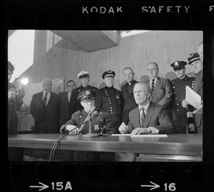 Police Patrolmen's Association President Daniel Sweeney and Mayor Kevin White signing new wage package for Boston Police. In background left to right, two unidentified men, Officer Ray Winston, Deputy Supt. William Bradley, Rev. James Lane, Com. Edmund McNamara, Patrolman Paul Whelan, Superintendent-in-Chief William Taylor, and Attorney Robert Wise