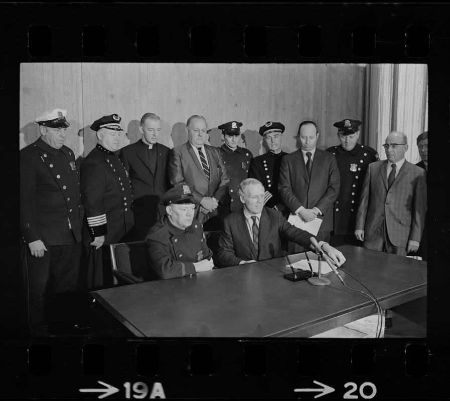 Police Patrolmen's Association President Daniel Sweeney and Mayor Kevin White signing new wage package for Boston Police. In background left to right, Officer Ray Winston, Deputy Supt. William Bradley, Rev. James Lane, Com. Edmund McNamara, Patrolman Paul Whelan, Superintendent-in-Chief William Taylor, Attorney Robert Wise, and three unidentified men