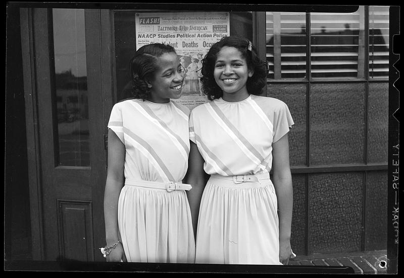 Two young women pose in front of newspaper