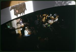 People eating at a restaurant, a sign of a cow in foreground