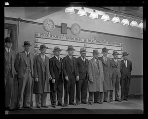 A group of men standing in front of a police department "lineup" board