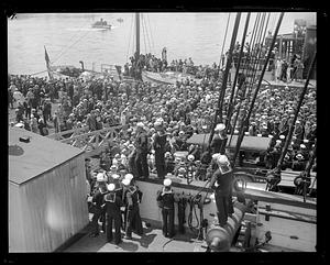 Sailors looking out from the deck of a ship, probably the USS Constitution, at a crowd on the dock