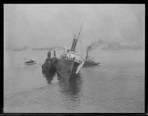 Merchants and Miners Co. freighter Ontario aflame after blasts, is pushed away from waterfront to the Bird Island flats with crew huddled on deck.