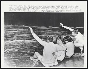 These four Long Beach State College students tempt fate as they dare tidal wave to engulfe them here early 3/28. L-R: Jerry Quinn, Jackie Butler, Beverly Blair, and John Carroll wait in the water for a tidal wave generated by a major earthquake in Alaska. However, nothing more that slightly higher than normal waves reached Southern California.