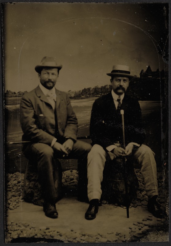 Studio portrait of two middle-aged gentleman in suits, hats and walking sticks
