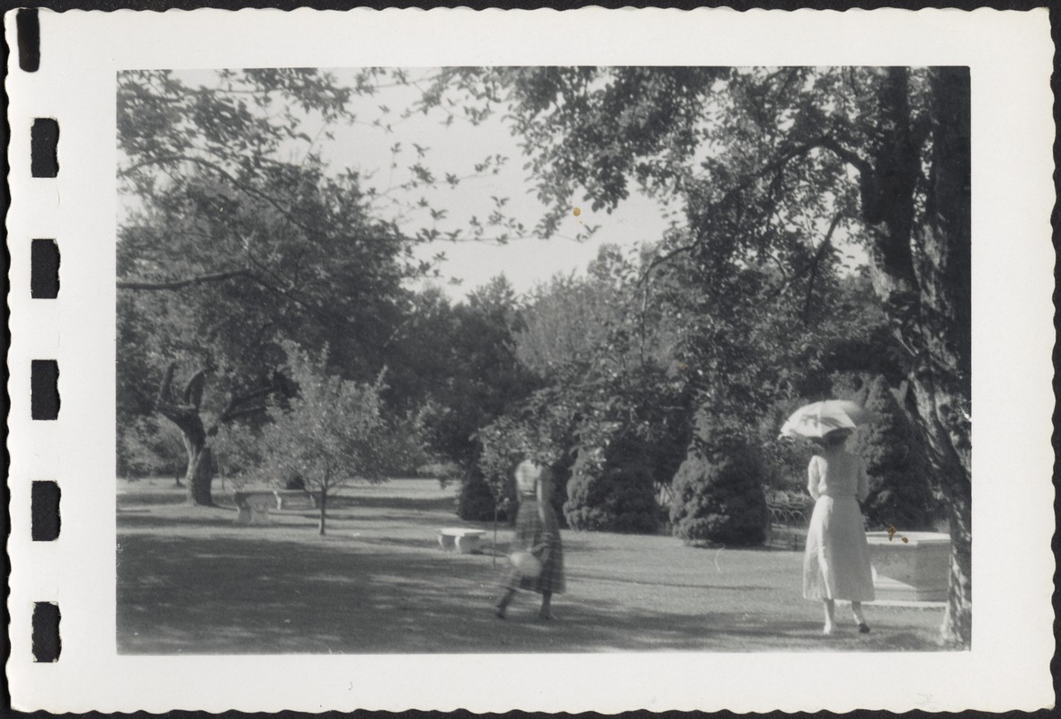 Two women (one with parasol) walking on grounds