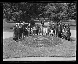 People standing around a flowerbed showing a symbol, possibly the square and compass