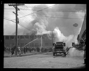 Spectators watch as firefighters using water hoses on a burning building