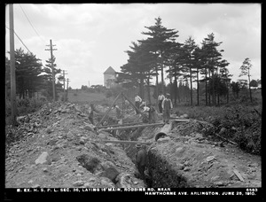 Distribution Department, Northern Extra High Service Pipe Lines, Section 36, laying 16-inch main in Robbins Road, near Hawthorne Avenue; Arlington Standpipe in background, center, Arlington, Mass., Jun. 25, 1910