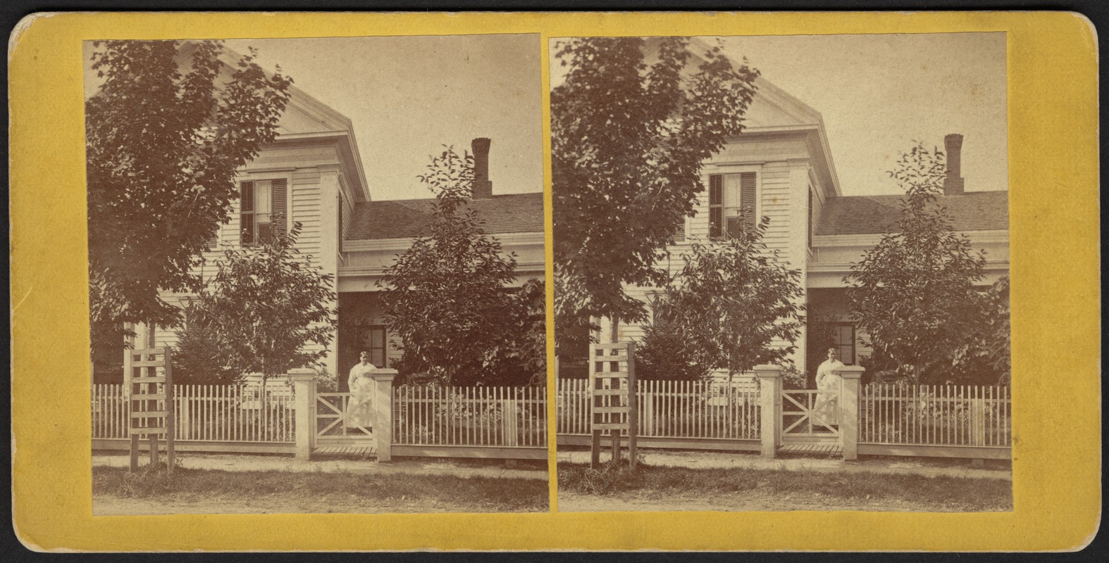 Woman standing outside of house and behind fence - Digital Commonwealth