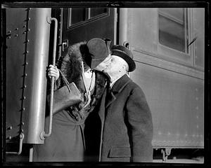 A woman standing on a train leaning down to kiss a man